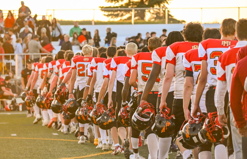 Rebels players lined up together, holding their helmets at sunset